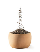 Black chia seeds falling into a wooden bowl, isolated on white background