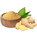 Ginger root powder in a wooden bowl with fresh ginger root slices and green leaves