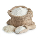 White rice flour in burlap sack with wooden scoop and raw rice on white background